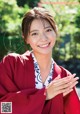 A woman in a red kimono smiles at the camera.