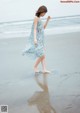 A woman in a blue dress walking on the beach.