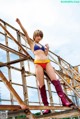 A woman in a bikini and boots posing on a metal structure.