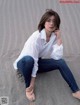 A woman sitting on the ground wearing a white shirt and jeans.